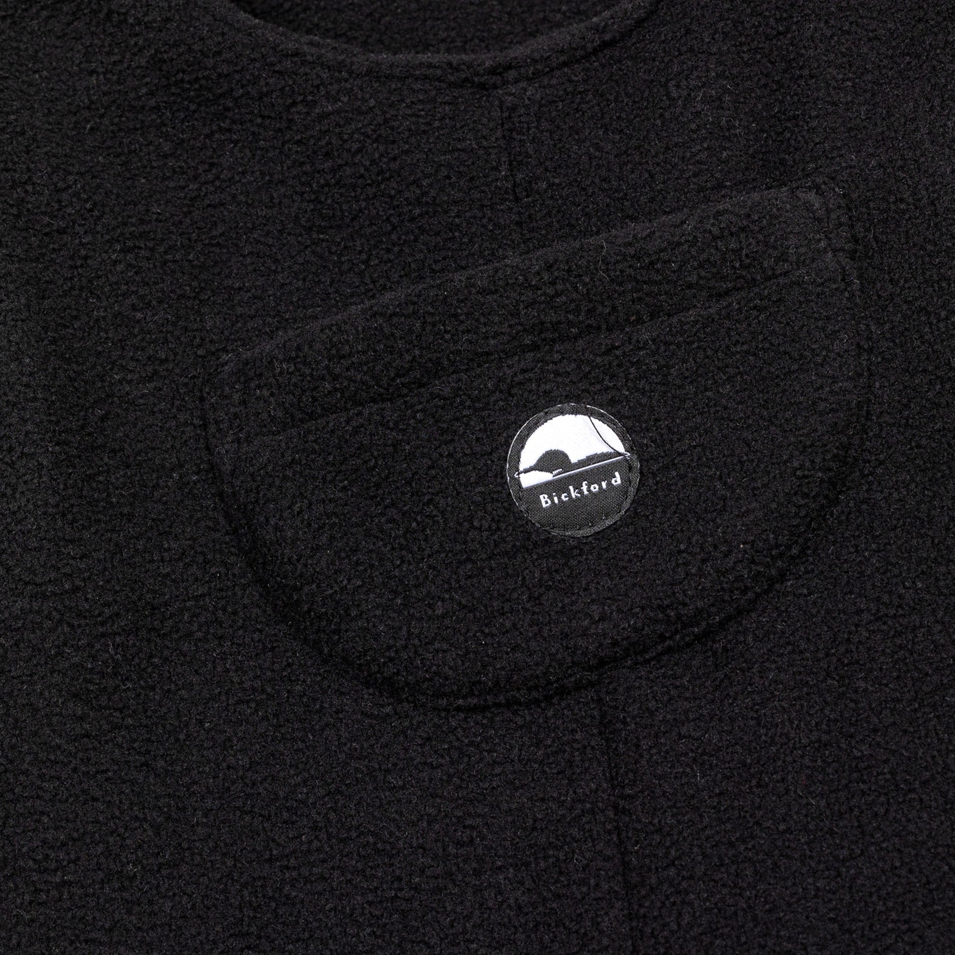 Close-up of the chest bib pocket on the black Youth Overalls showing the circular woven Bickford mountain logo patch centered on the pocket.