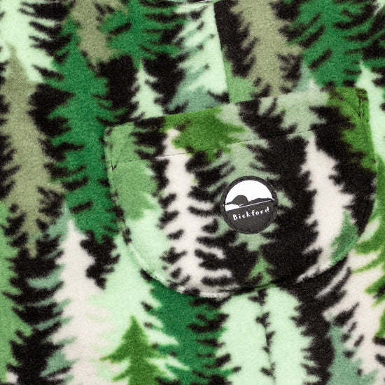 Close-up of the chest bib pocket on the Eastern Pine Youth Overalls showing the circular woven Bickford mountain logo patch centered on the pocket against the pine tree print.