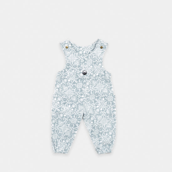 Bickford USA Youth fleece overalls in the Snowflake colorway, laid flat on a light gray background, featuring an all-over ornate snowflake and medallion print in grey and white, with brass snap shoulder straps, a chest bib pocket with circular Bickford logo patch, two side pockets, and elasticized ankle cuffs.