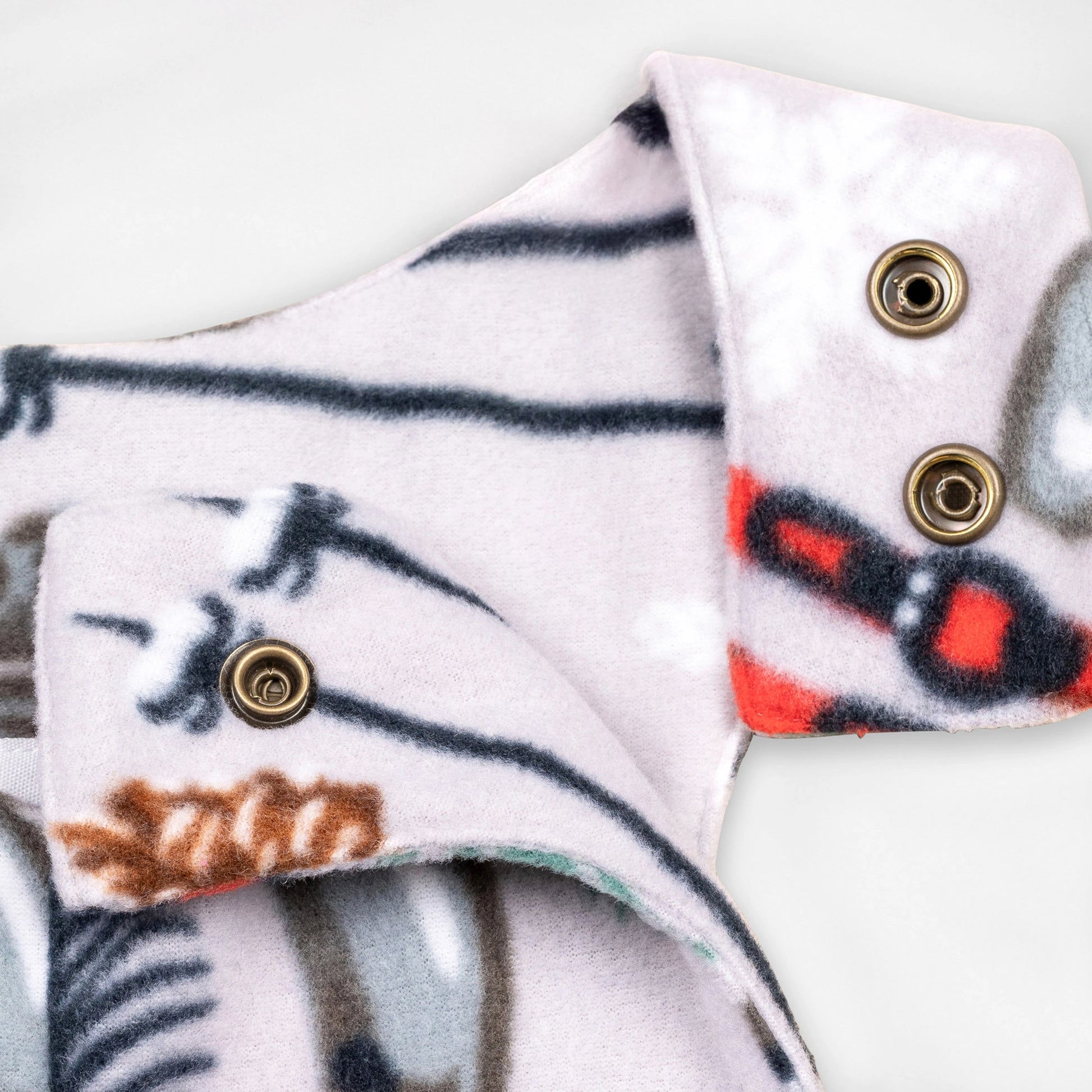 Close-up detail of the Sugarbush Youth Overalls showing the adjustable shoulder straps with brass snap closures against the winter sports print featuring skis, poles, and ice skates.
