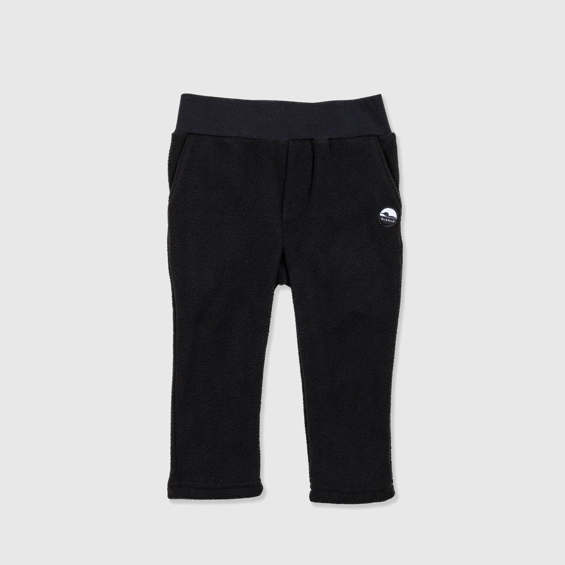 Bickford USA Youth fleece pants in solid black, laid flat on a light gray background, showing the full front with a wide elastic waistband, side hand pockets, and circular Bickford logo patch on the hip.