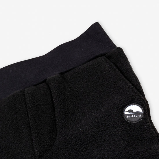 Close-up detail of the black Youth Pants showing the wide black elastic waistband, the angled side pocket opening, and the circular woven Bickford mountain logo patch.

