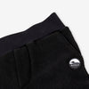 Close-up detail of the black Youth Pants showing the wide black elastic waistband, the angled side pocket opening, and the circular woven Bickford mountain logo patch.

