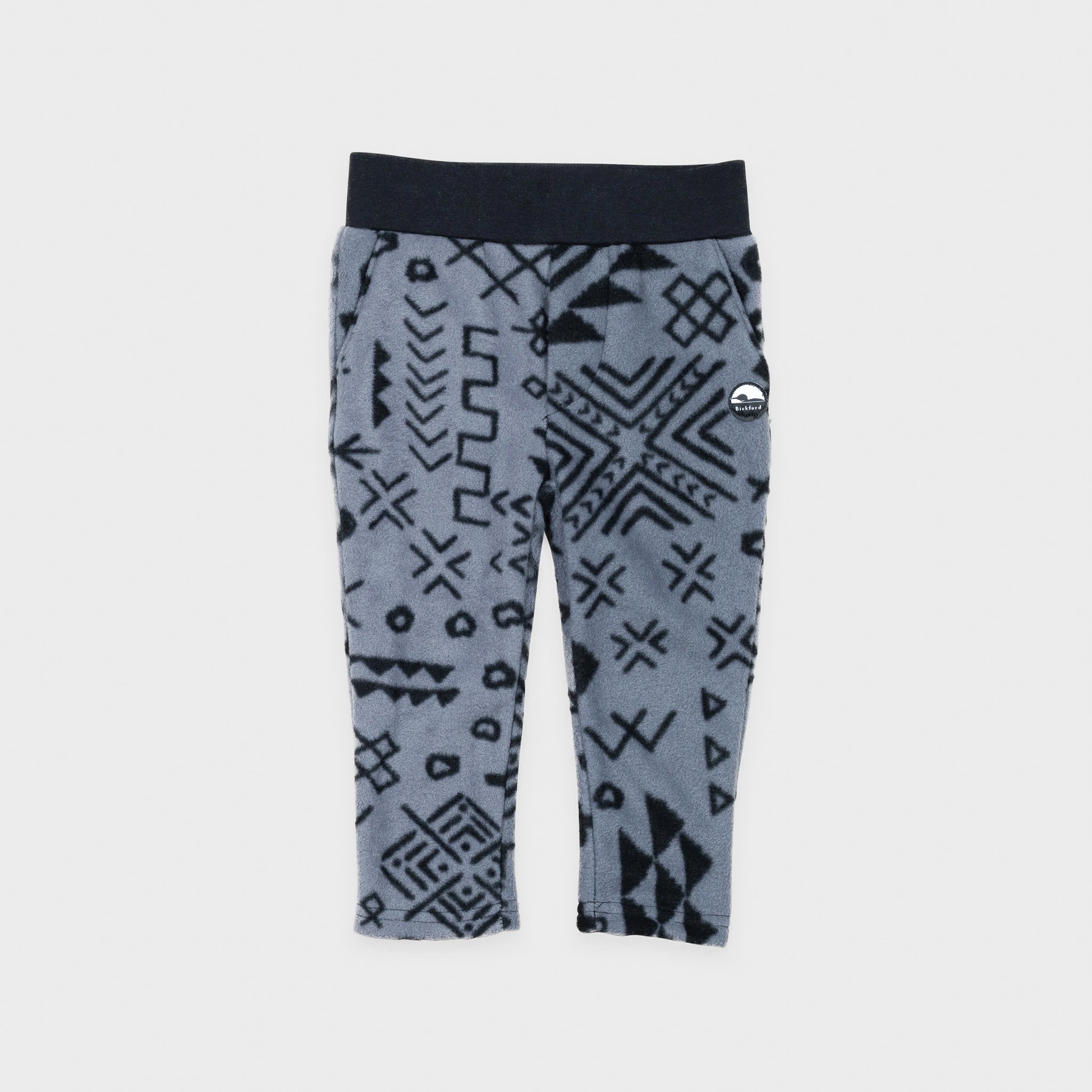 Bickford USA Youth fleece pants in the Boulder colorway, laid flat on a light gray background, featuring an all-over black geometric tribal print on a grey background, with a wide black elastic waistband, side hand pockets, and circular Bickford logo patch on the hip.