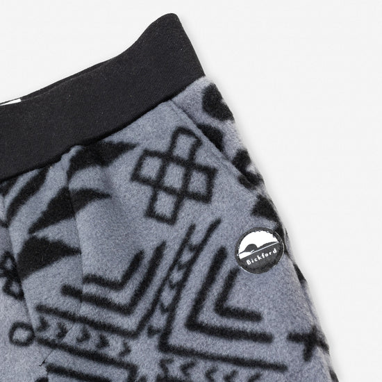 Close-up detail of the Boulder Youth Pants showing the wide black elastic waistband, the angled side pocket, and the circular woven Bickford mountain logo patch against the grey and black geometric tribal print.