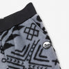 Close-up detail of the Boulder Youth Pants showing the wide black elastic waistband, the angled side pocket, and the circular woven Bickford mountain logo patch against the grey and black geometric tribal print.