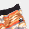 Close-up detail of the Heritage Trail Youth Pants showing the wide black elastic waistband, angled side pocket, and circular woven Bickford mountain logo patch against the southwestern stripe and geometric print in orange, brown, and grey.