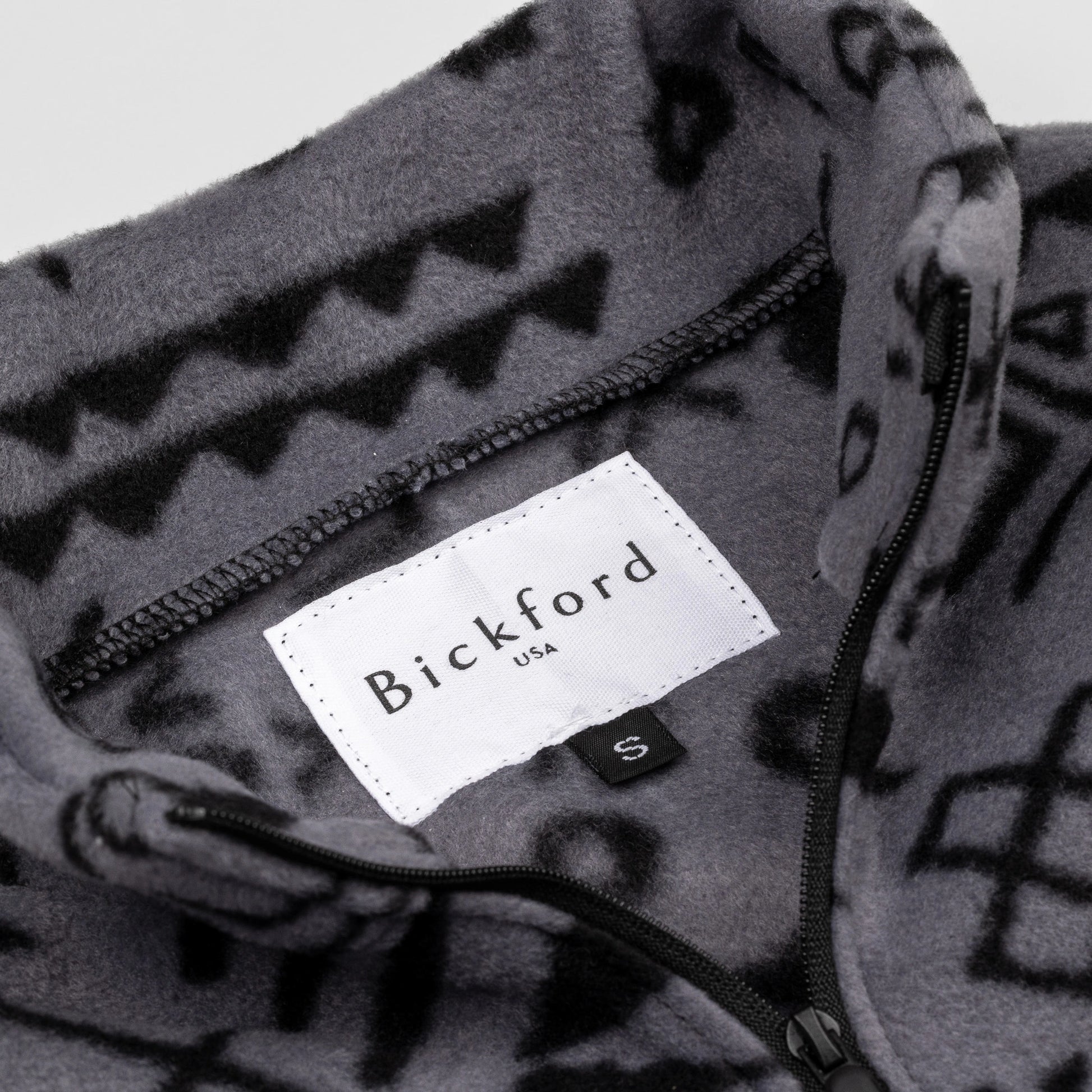 Close-up detail of the Boulder Youth Quarter-Zip showing the open funnel collar with the Bickford USA label and size tag visible, revealing the geometric tribal print on the inner collar and the black zipper.