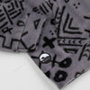 Close-up of the lower hem corner of the Boulder Youth Quarter-Zip showing the circular woven Bickford logo patch with a mountain graphic, set against the grey and black geometric print.