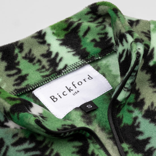 Close-up detail of the Eastern Pine Youth Quarter-Zip showing the open funnel collar with the Bickford USA label and size tag visible, with the pine tree print visible on the inner collar and the black zipper.