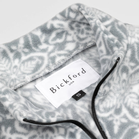 Close-up detail of the Snowflake Youth Quarter-Zip showing the open funnel collar with the Bickford USA label and size tag visible, with the grey and white medallion print visible on the inner collar and the black zipper.