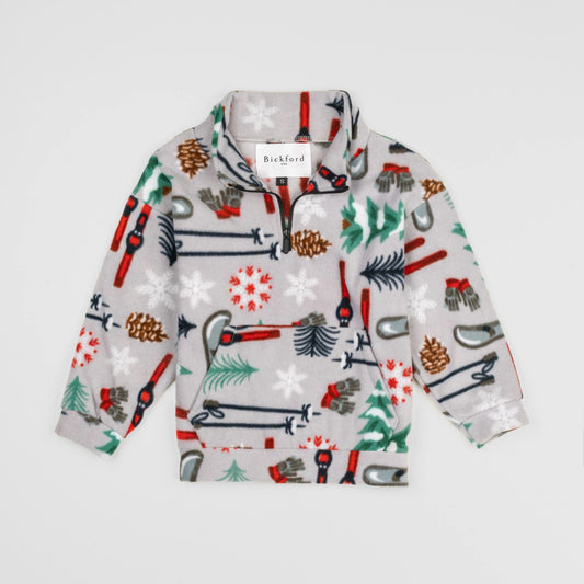 Bickford USA Youth Quarter-Zip fleece pullover in the Sugarbush colorway, laid flat on a light gray background, featuring an all-over winter sports print with skis, ski poles, ice skates, mittens, snowflakes, pinecones, and pine trees on a light grey background, with a funnel collar, quarter-zip closure, and front kangaroo pocket.