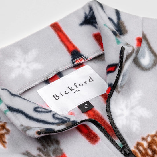 Close-up detail of the Sugarbush Youth Quarter-Zip showing the open funnel collar with the Bickford USA label and size tag visible, with the winter sports print visible on the inner collar and the black zipper.