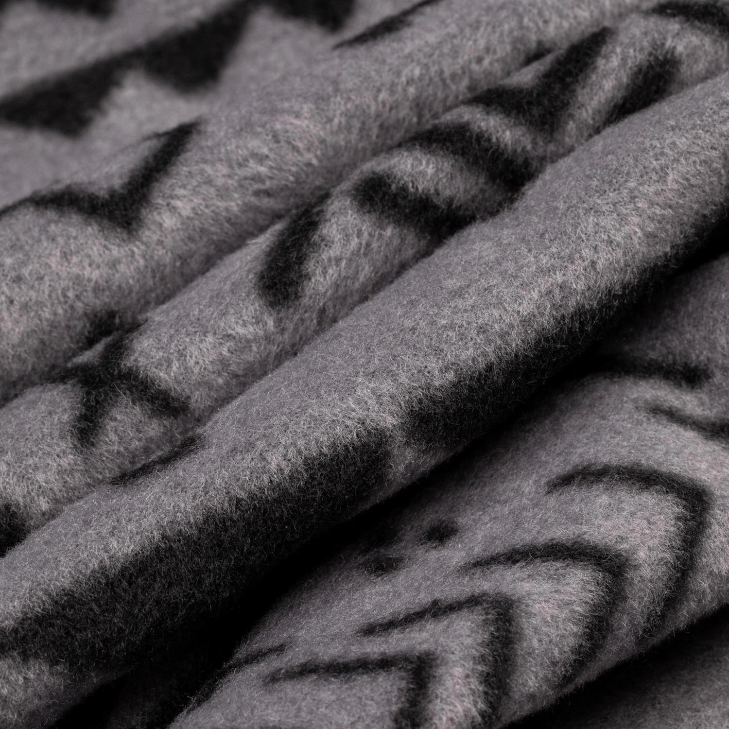 Close-up macro shot of soft fleece fabric in the Boulder colorway — a gray base with a black allover geometric and tribal print — showing the plush texture and depth of the pile.