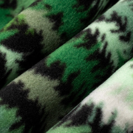 Close-up macro shot of fleece fabric in the Eastern Pine colorway — a forest print in deep green, light green, and white with black tree silhouettes — showing the plush texture and layered tones of the pattern.