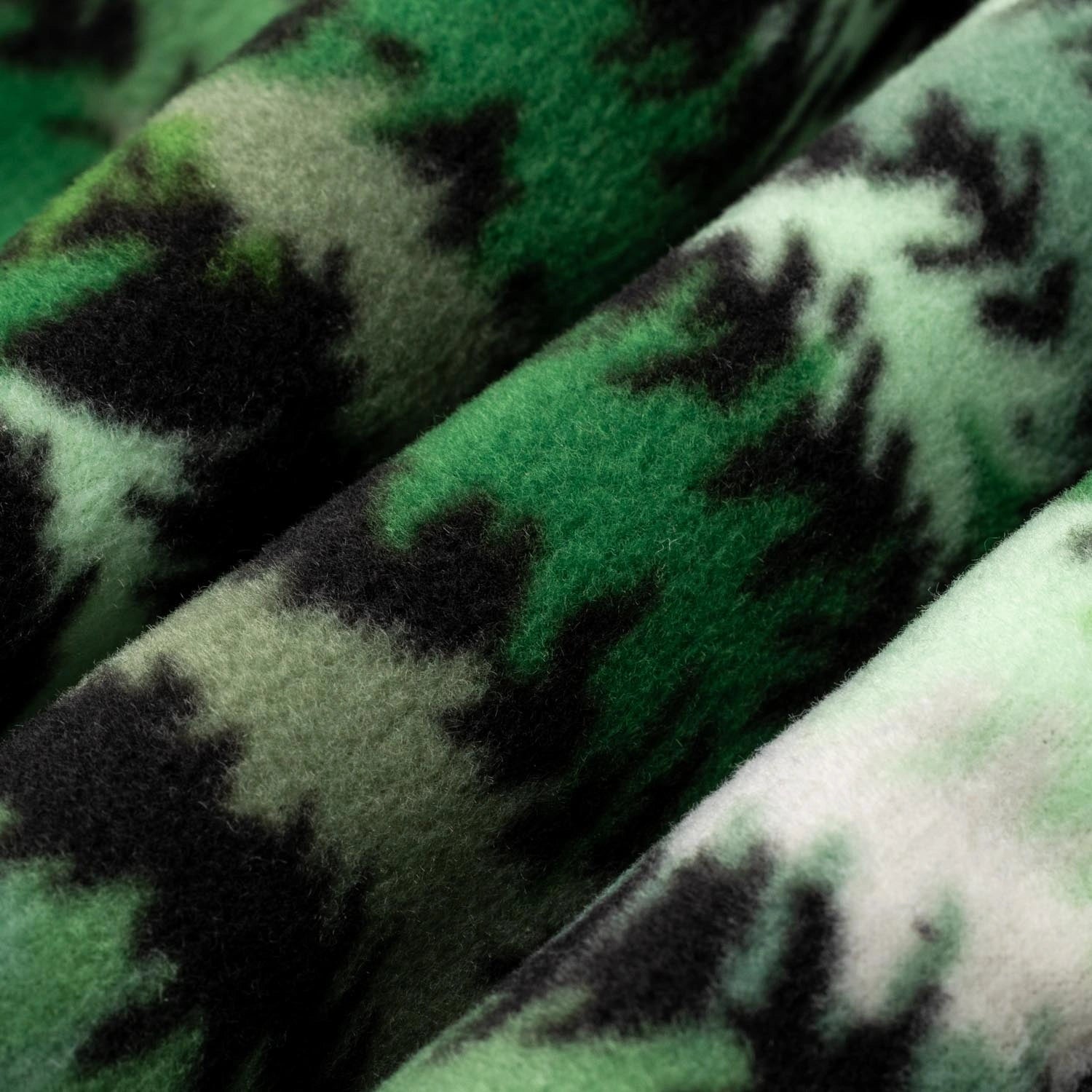 Close-up macro shot of fleece fabric in the Eastern Pine colorway — a forest print in deep green, light green, and white with black tree silhouettes — showing the plush texture and layered tones of the pattern.