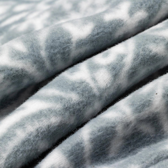 Close-up macro shot of fleece fabric in the Snowflake colorway — a soft blue-gray base with a white floral and snowflake lattice print — showing the delicate pattern and plush pile texture.