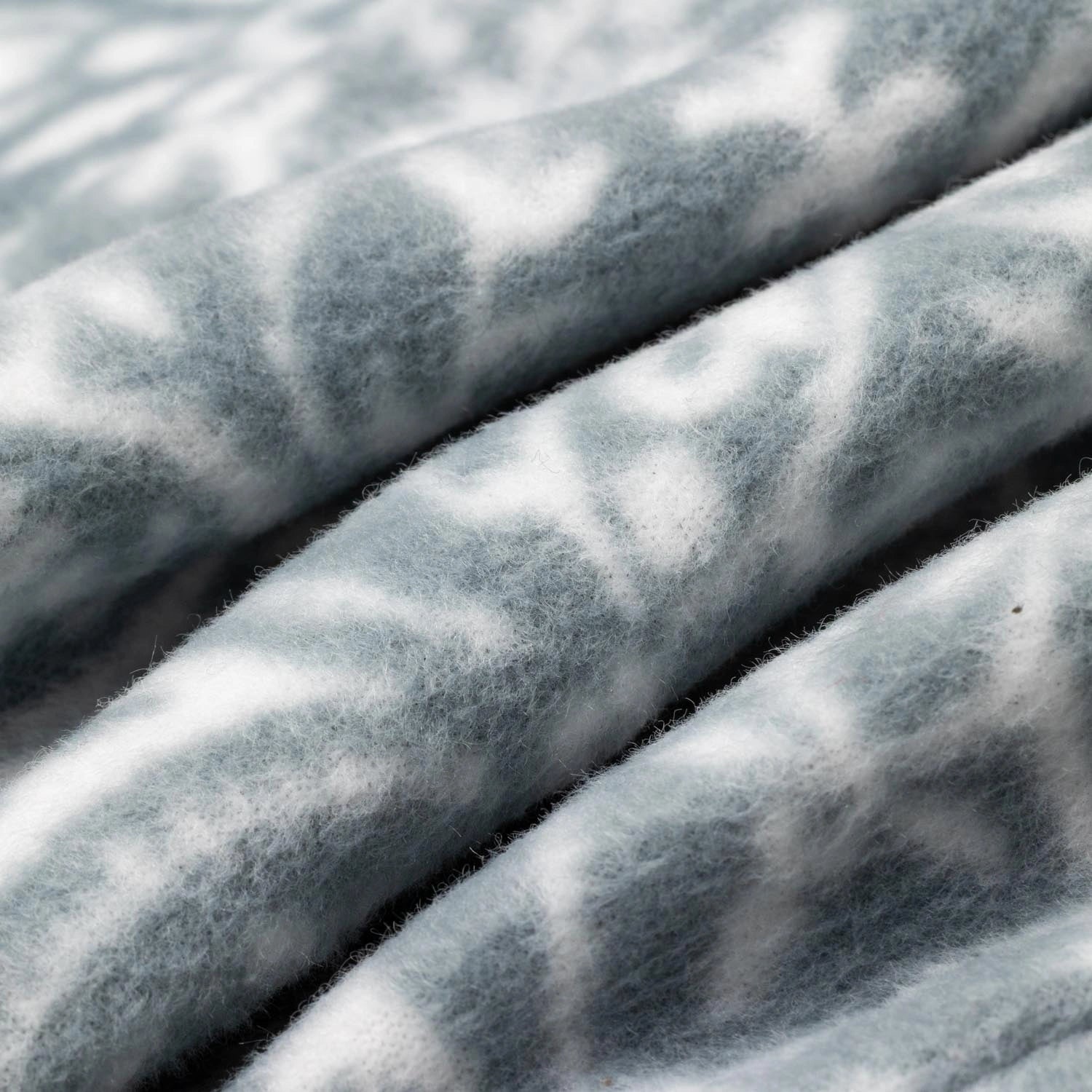Close-up macro shot of fleece fabric in the Snowflake colorway — a soft blue-gray base with a white floral and snowflake lattice print — showing the delicate pattern and plush pile texture.