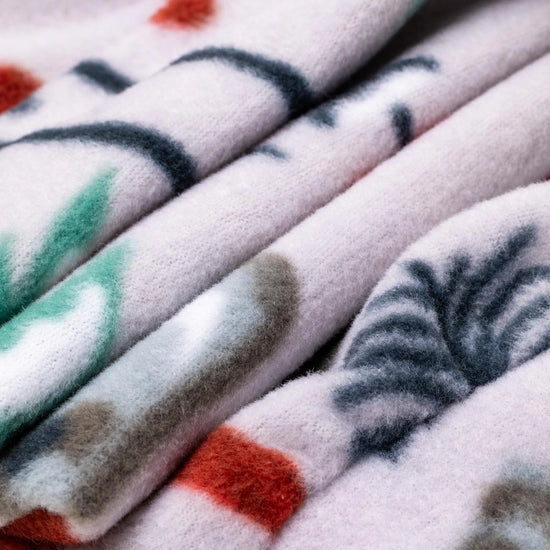 Close-up macro shot of fleece fabric in the Sugarbush colorway — a white base with a scattered winter ski resort print including evergreen trees, pine cones, skis, and red accents — showing the fine detail and soft pile texture.